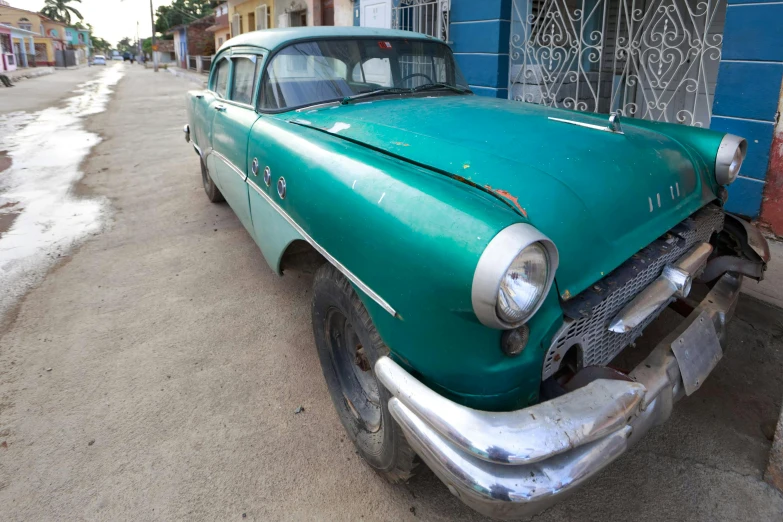 an old green car parked on the side of the street