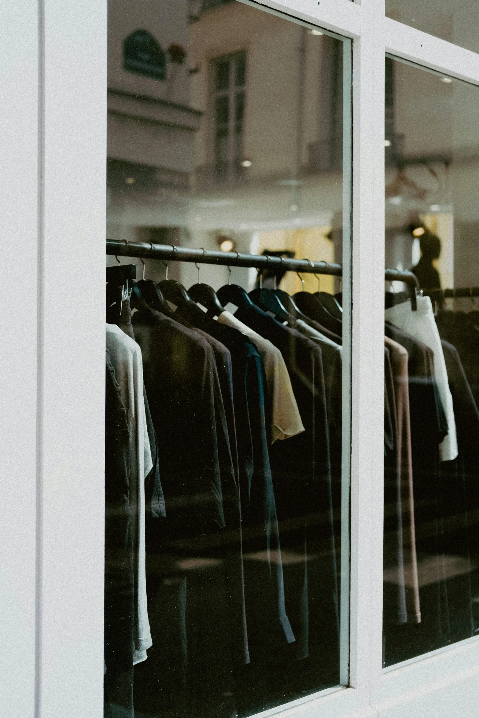 clothing on racks in a window with other clothes hanging behind them