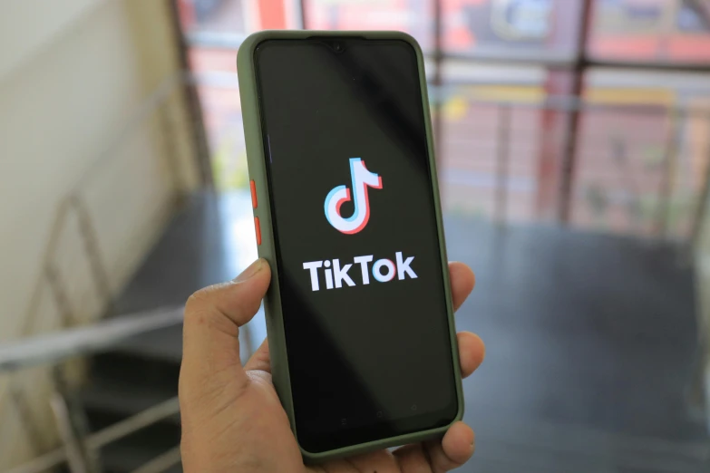 a person holding a smart phone that says tiktok on the display