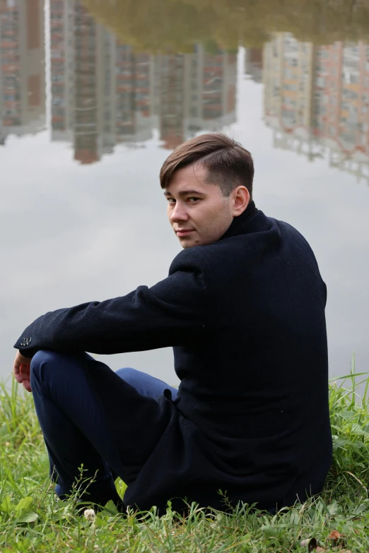 a man sitting on the ground in front of a body of water