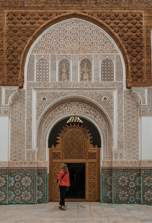 a woman in a red coat stands on a stone walkway in front of a colorful archway