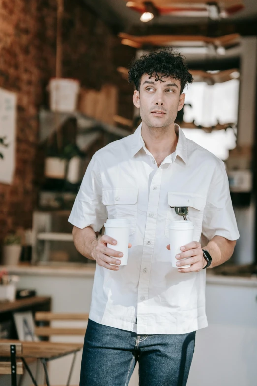 a man in white shirt holding two cups of coffee