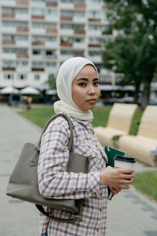 a young woman standing in front of a park holding a cup