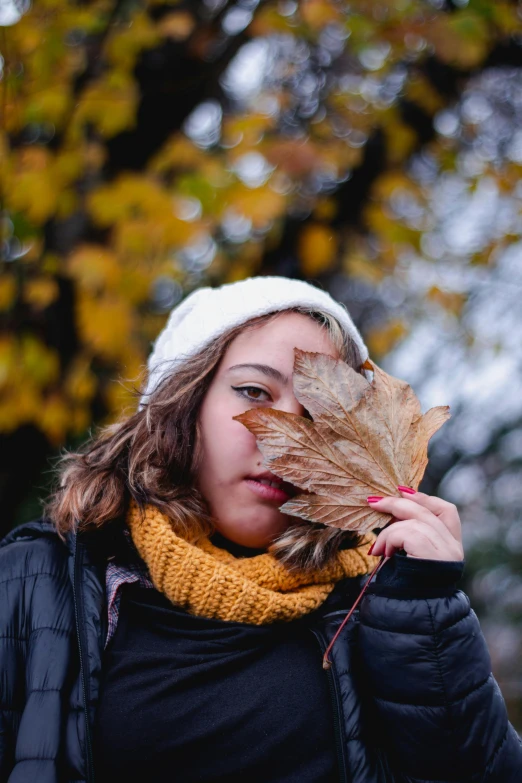 a woman wearing a white beanie holding a dry leaf