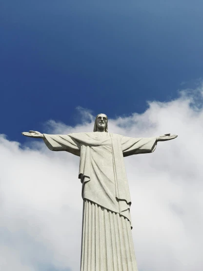 a statue of jesus in the air with clouds behind it