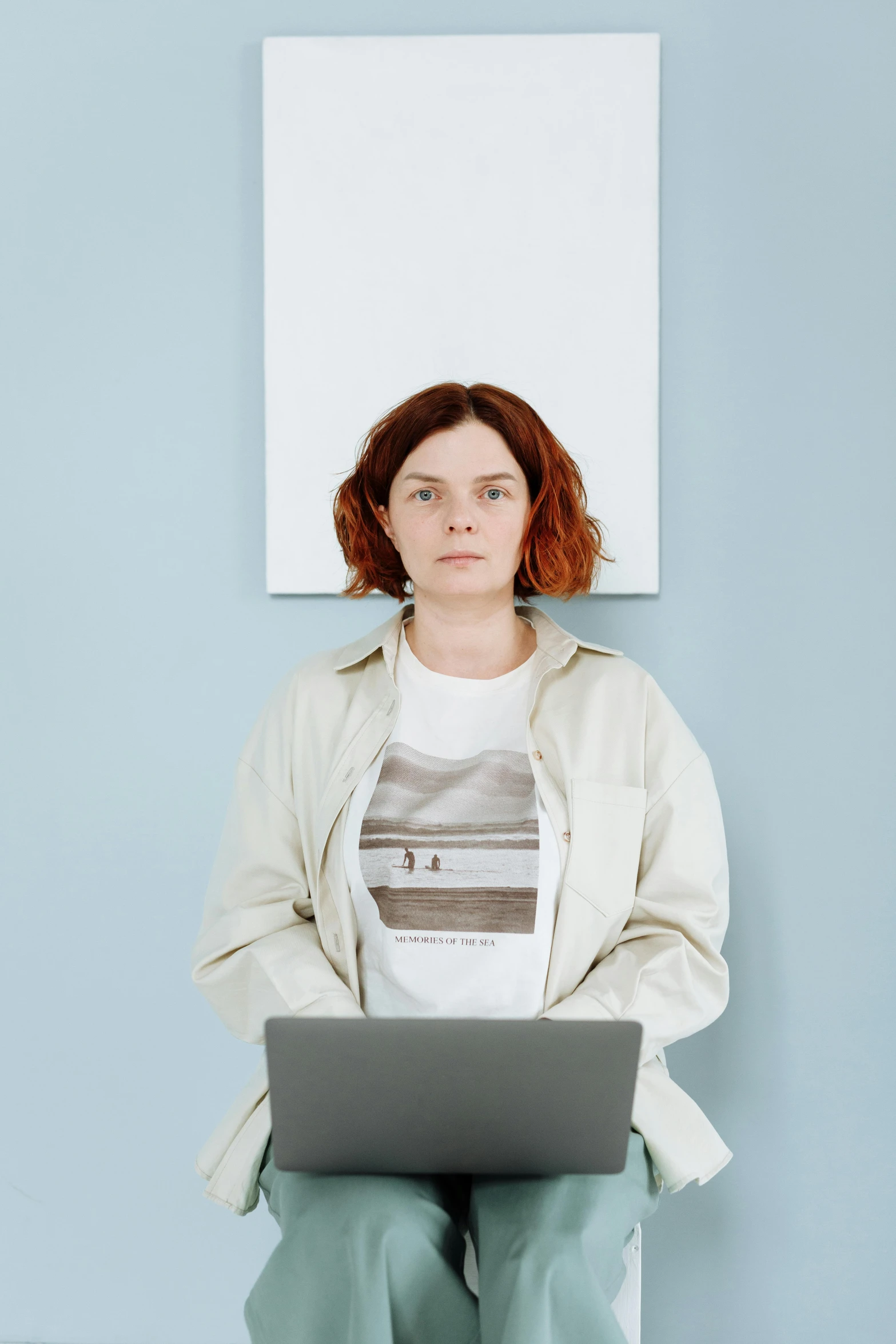 a woman sitting in front of a painting holding a laptop