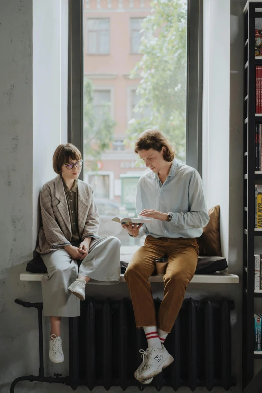 the man is reading while the woman is sitting in front of the window