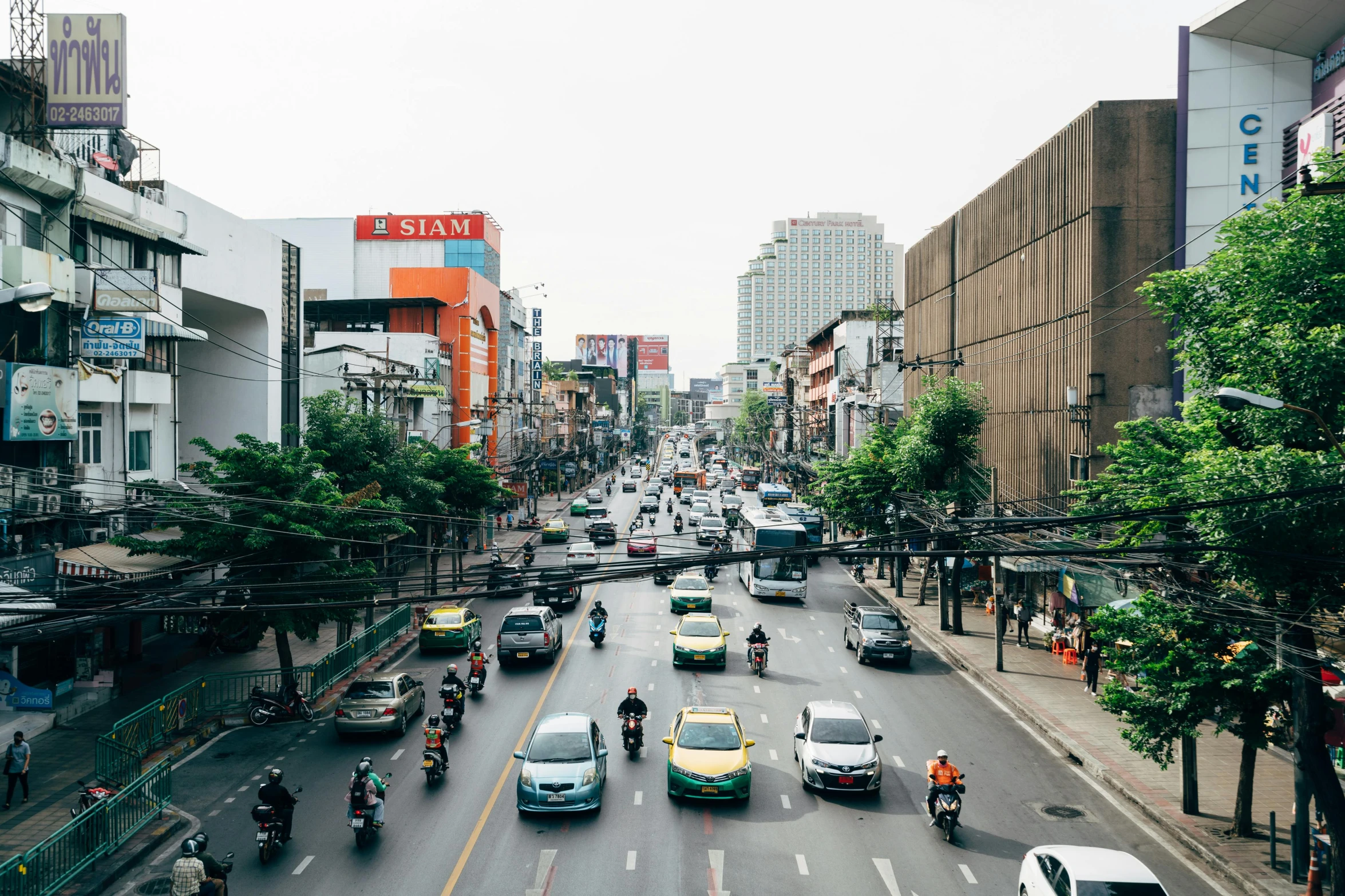 an overhead view of city street, with people on motor bikes and traffic, in front of many buildings