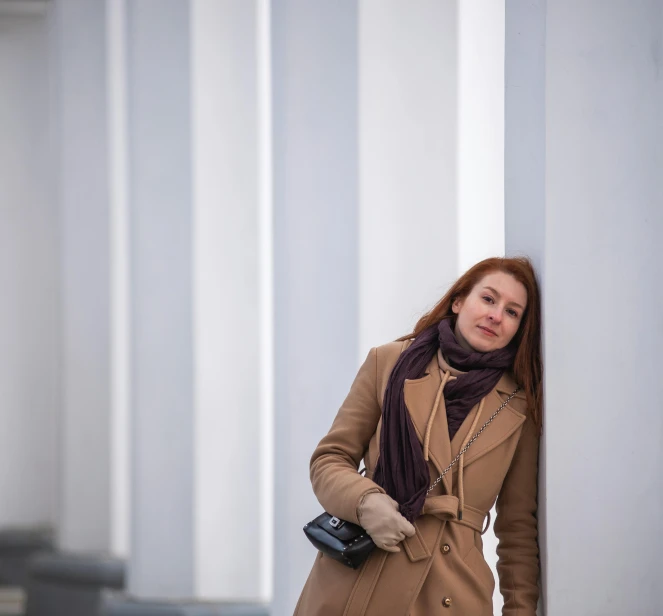 woman in coat and scarf leaning against column