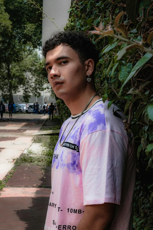 a guy posing with a phone and in front of bushes