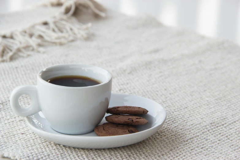 two chocolate covered cookies are placed on a plate beside a cup of coffee