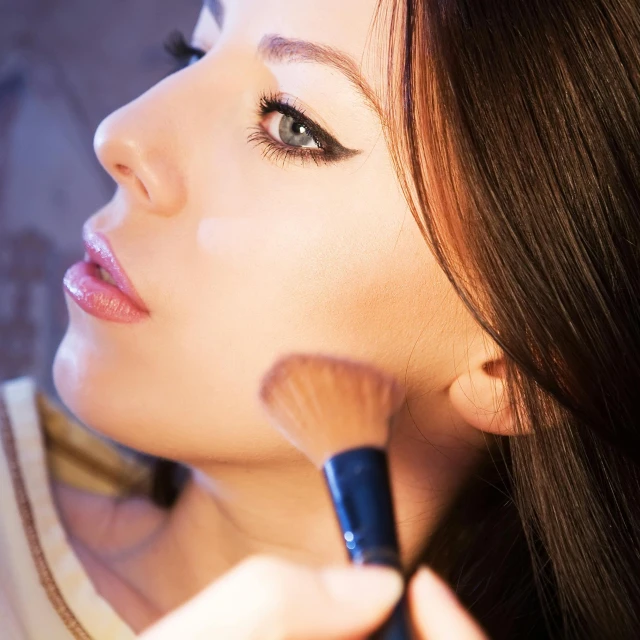 a woman holding a brush and applying makeup on her face