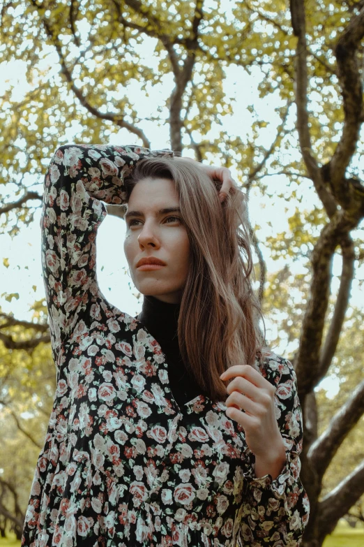 a woman standing next to a tree holding her hand over her head