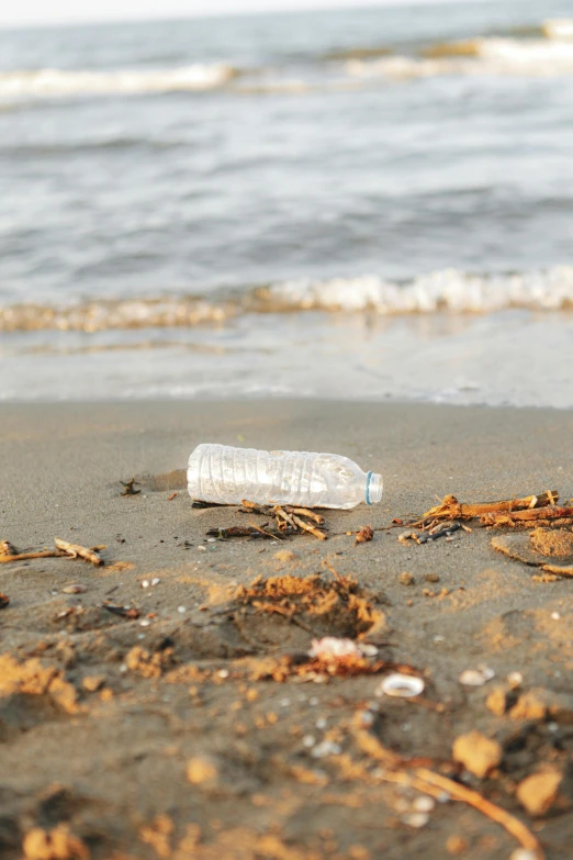 empty white plastic bottle sitting in the sand near a body of water