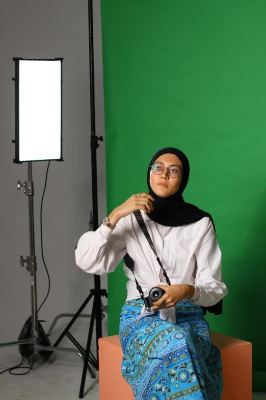 an arabic model with head scarf, white shirt and glasses holding camera