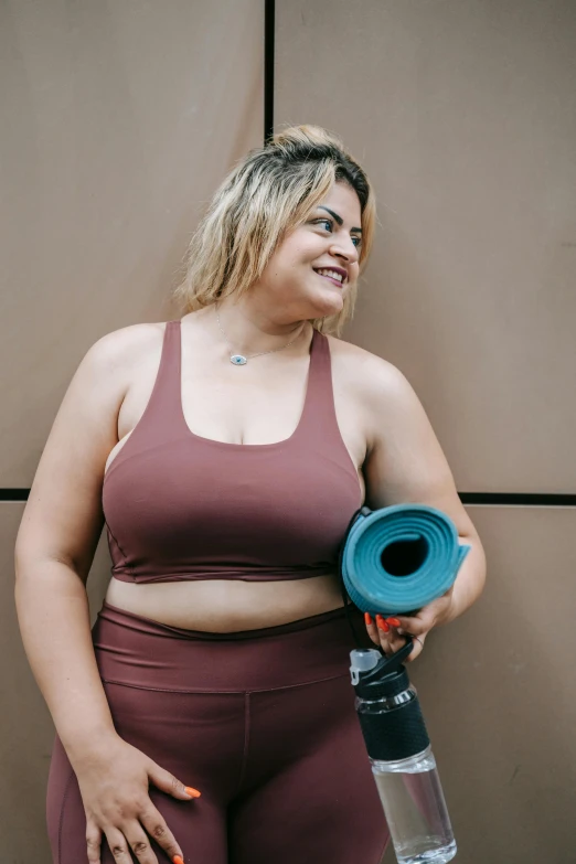 a woman wearing a sports  and yoga pants holding a water bottle and smiling