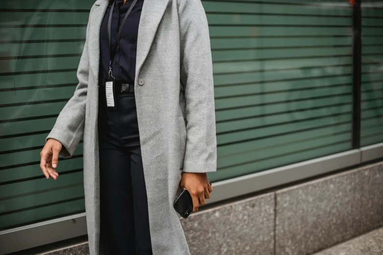 woman wearing coat and dress pants holding handbag standing outside