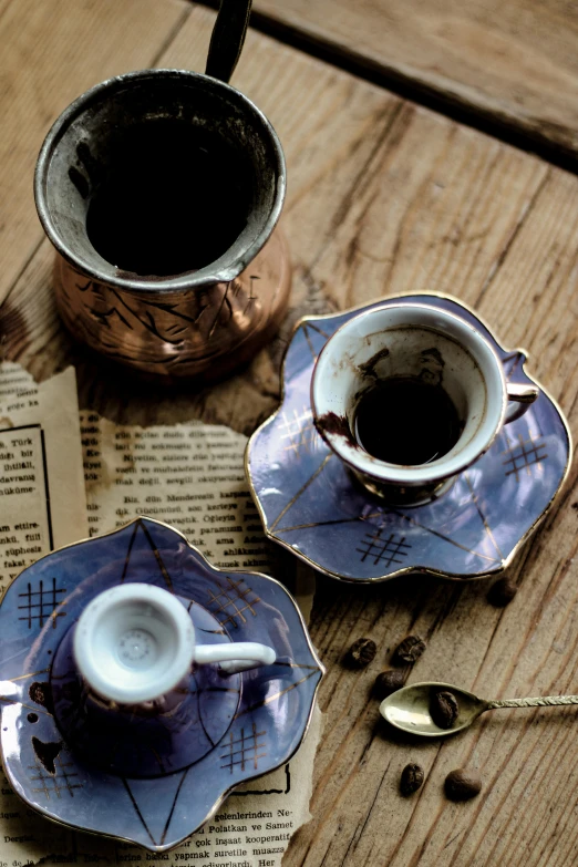 a wooden table topped with two coffee cups and saucers