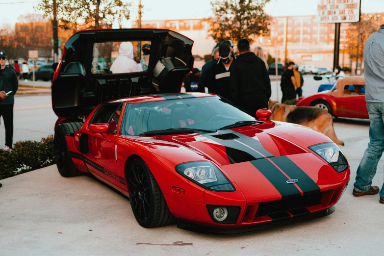 the red and black sports car is parked next to some people