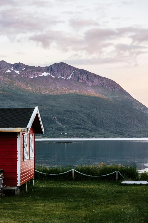 a red hut sitting in the grass by the lake