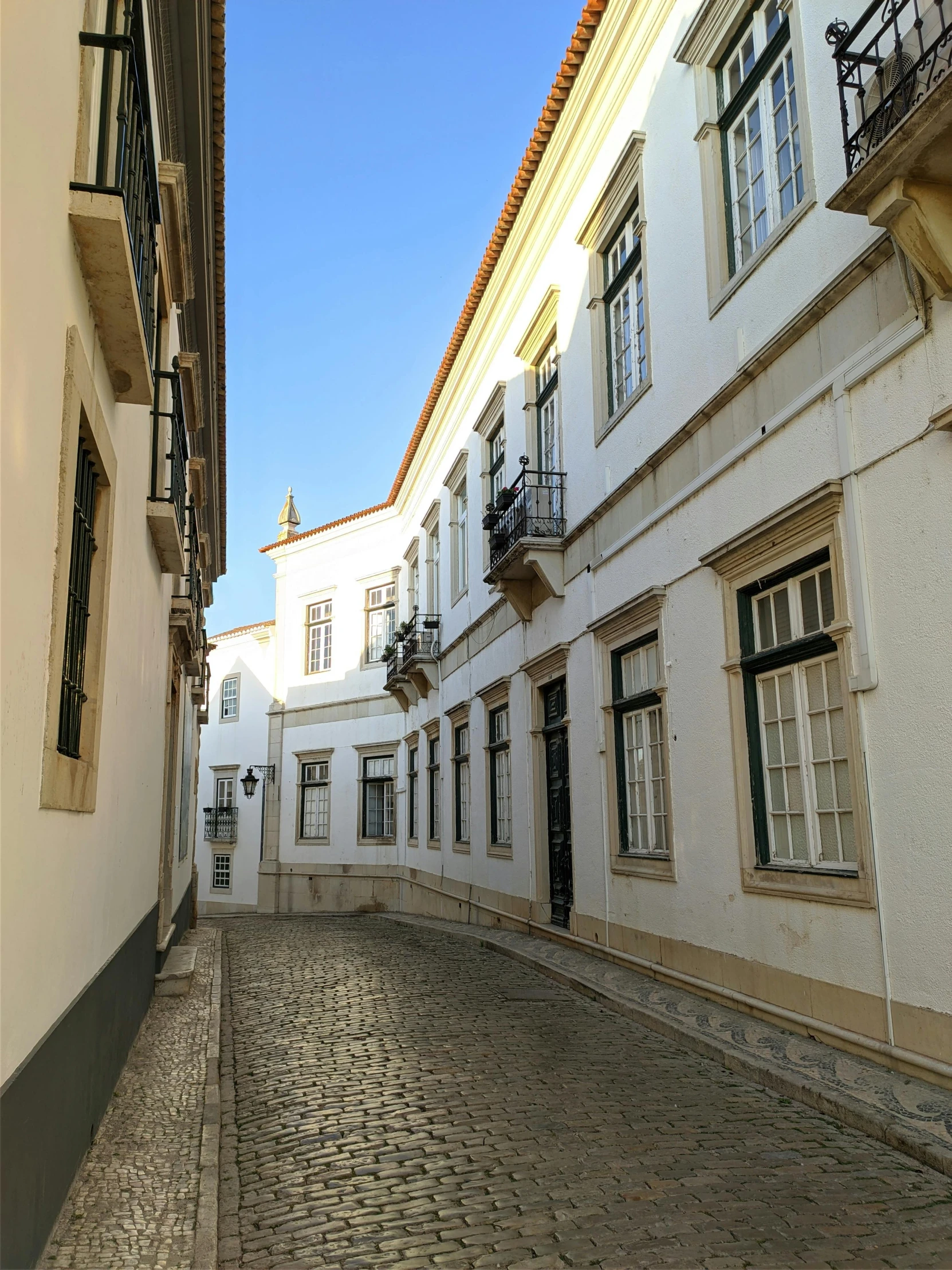 a small narrow street is flanked by white building