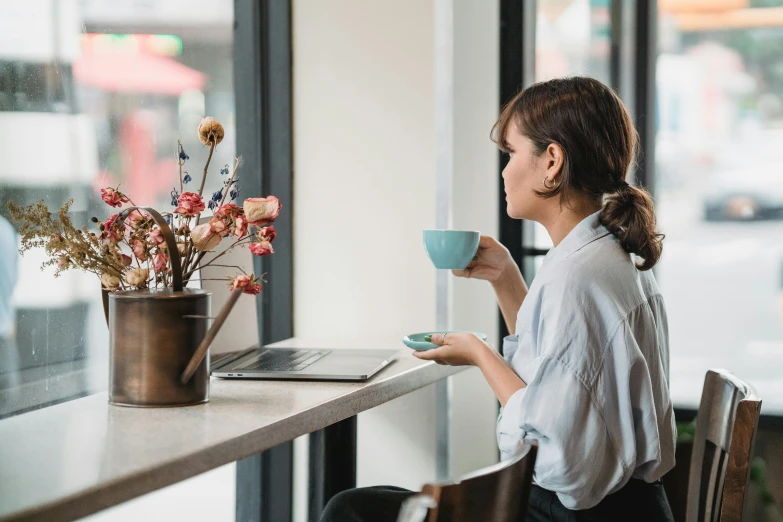 woman drinking coffee at a table next to a laptop