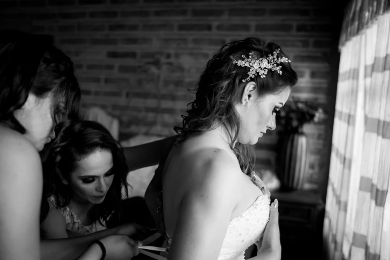 two woman in wedding dresses, one of them helping her friend get into the dress