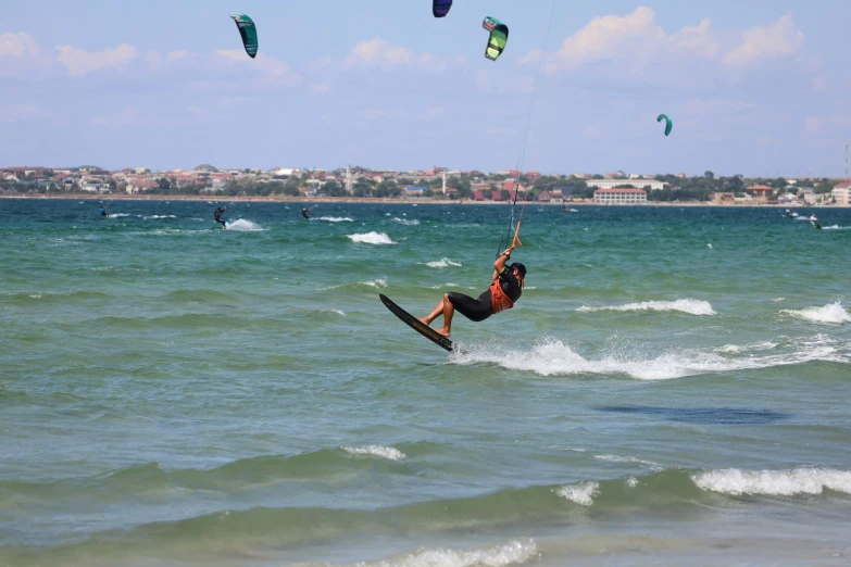 a person surfing on the ocean, with parasails in the sky