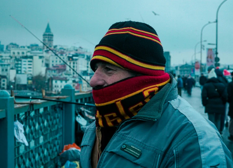 a man in a beanie and scarf stares at soing while holding his hand to his mouth