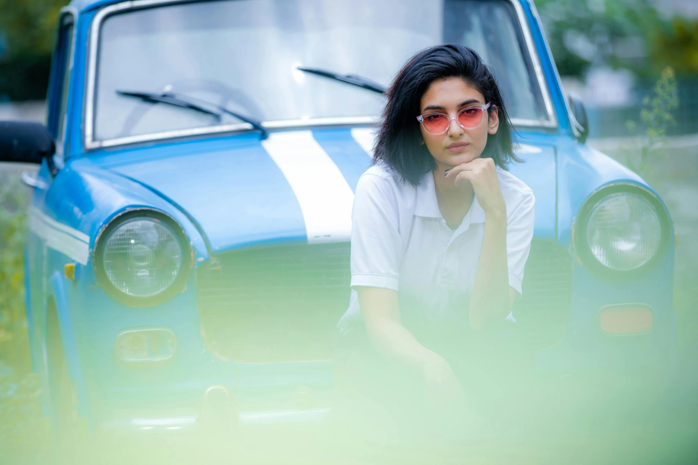 a woman in sunglasses poses next to a blue vintage car
