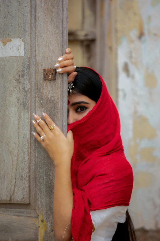 a woman wearing a scarf hiding behind the door of a barn