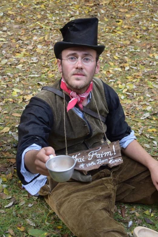 man in a black top hat holds up a sign and a bowl