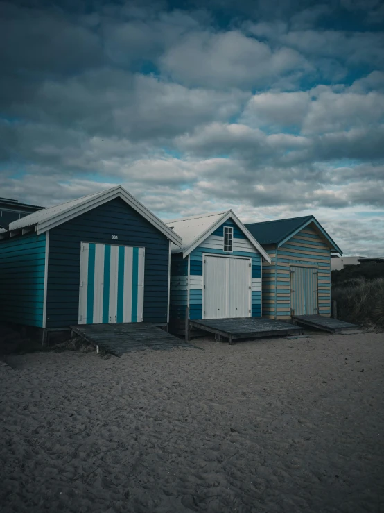 a line of blue beach houses next to each other on a sandy shore