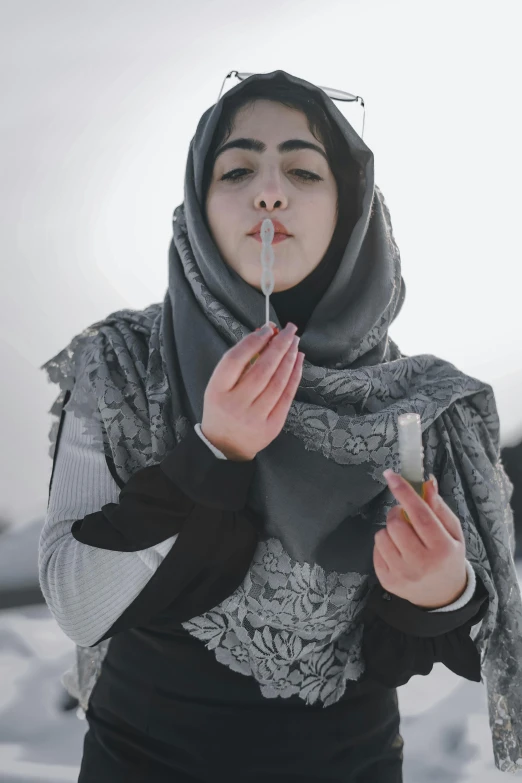 the woman with the scarf on her head holds a cigarette and looks at the camera