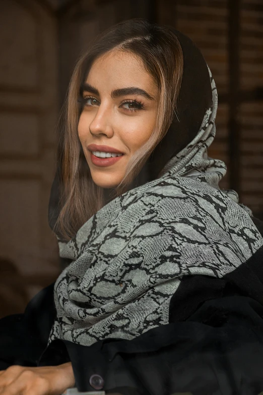 a smiling woman is wearing a scarf and holding her hands in front of her