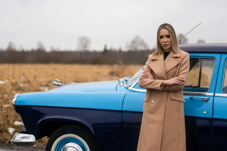 a woman wearing a trench coat standing next to a car