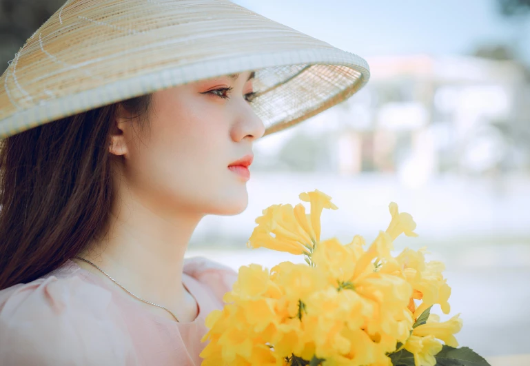 a woman wearing a large white hat holds a bunch of yellow flowers