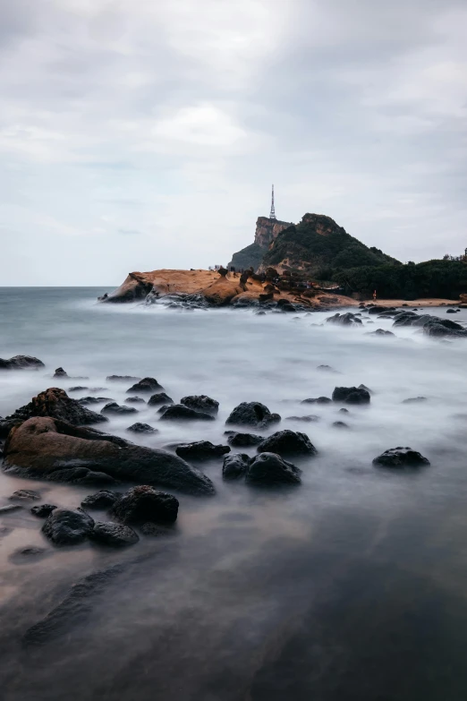 a rocky beach with lots of water in front of a light house