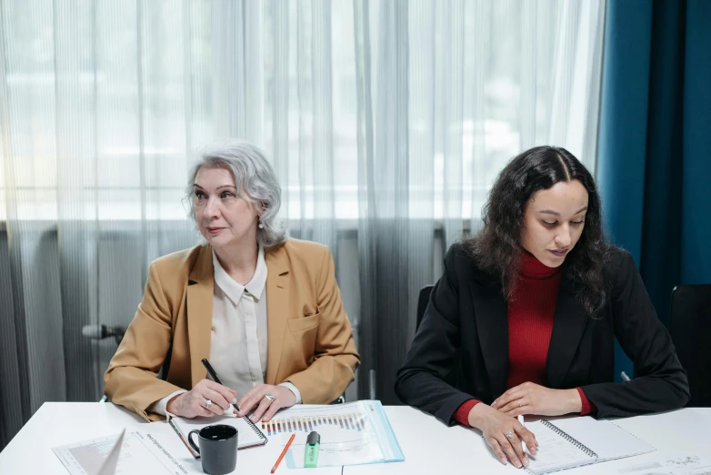 two women sitting at a white table doing paperwork