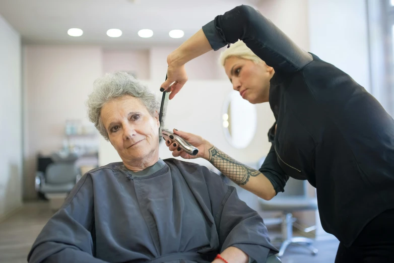 an elderly woman gets haircut while standing next to a female barber