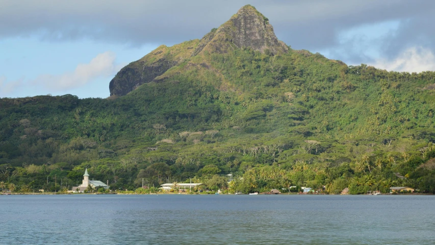 a mountain near some trees is next to water