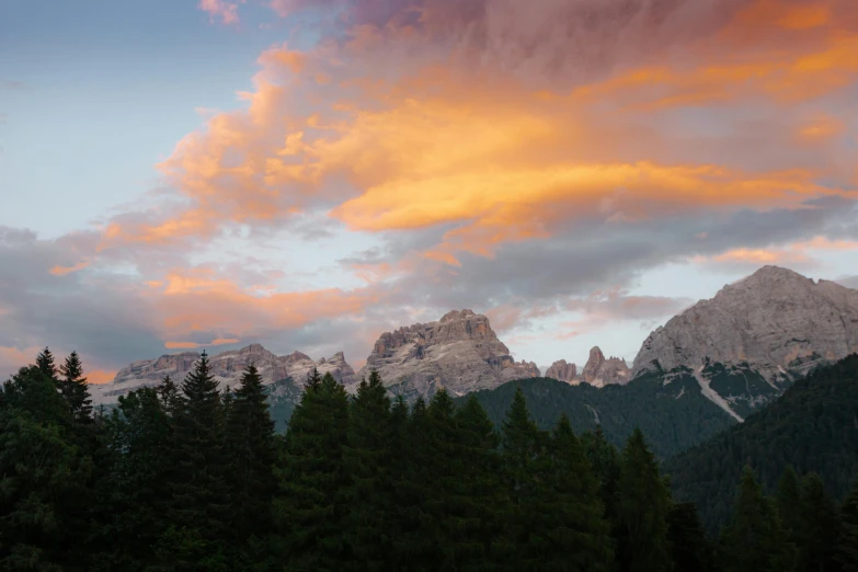 an orange and pink sky with clouds and trees