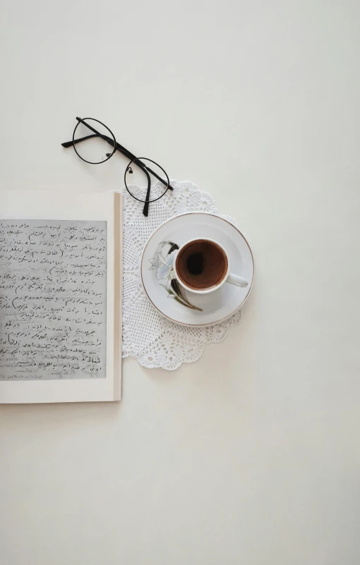 a cup of coffee next to a book with eyeglasses