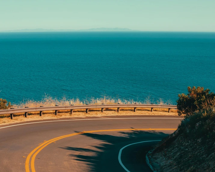 there is a curved road that runs along side the ocean