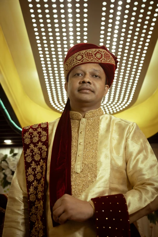 a young man dressed in a white and gold wedding outfit