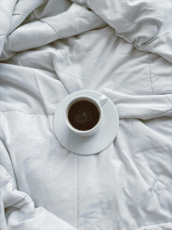 a coffee cup on a saucer on a bed comforter