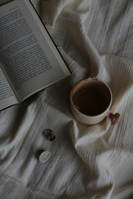 a cup of coffee and a book sit on a white blanket