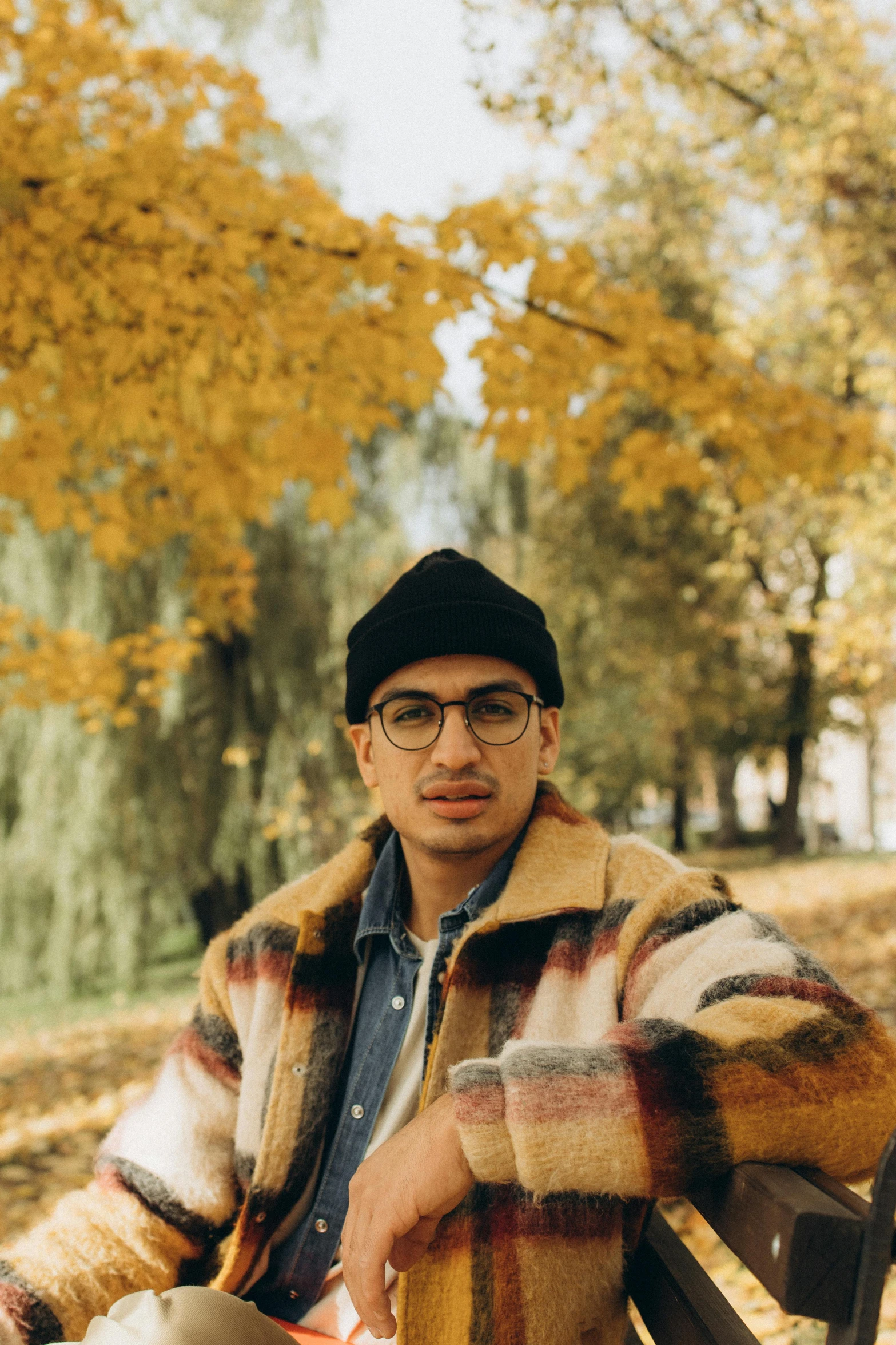 the man is sitting on a bench near fall leaves