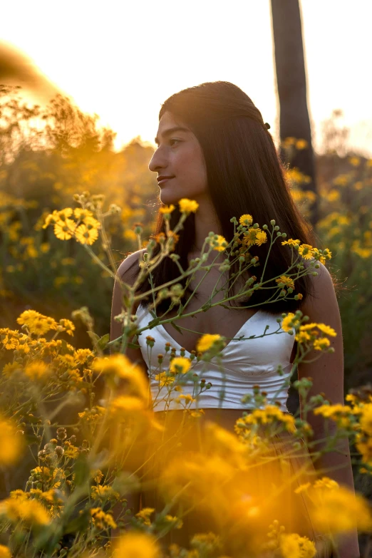 a woman standing in a field of wildflowers at sunset