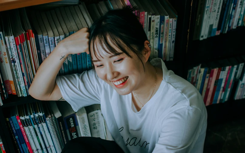 a woman smiling next to a book shelf filled with books